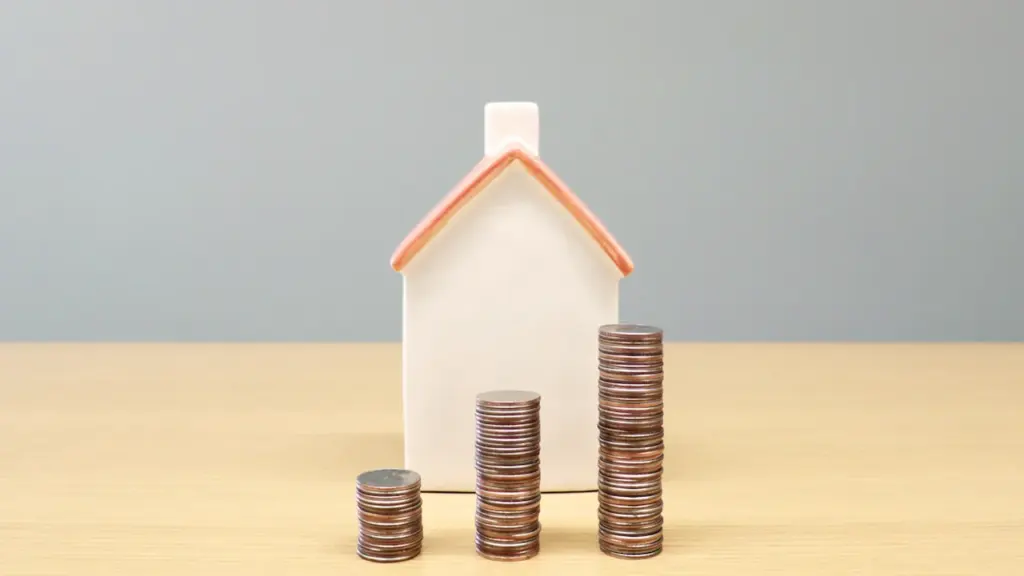 Une petite maison symbolique posée à côté de piles de pièces de monnaie.